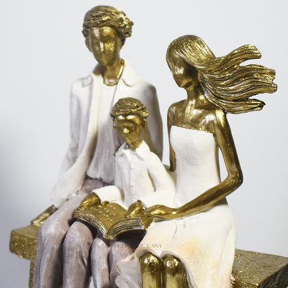 Escultura decorativa em resina representando pai, mãe e filho sentados em um banco lendo um livro, simbolizando união familiar e momentos de aprendizado.