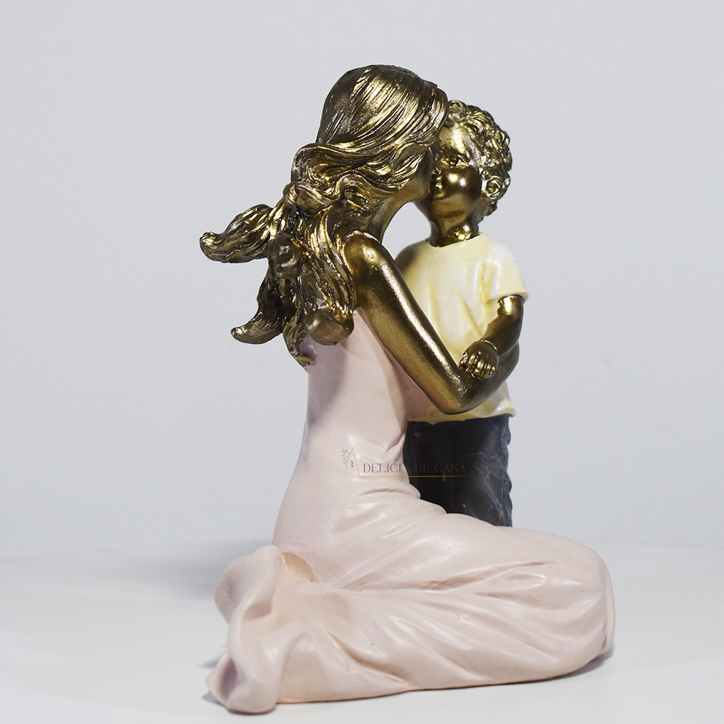 Escultura decorativa de mãe abraçando seu filho, confeccionada em resina com acabamento dourado, branco e cinza, medindo 11,5 x 11,5 x 8 cm.