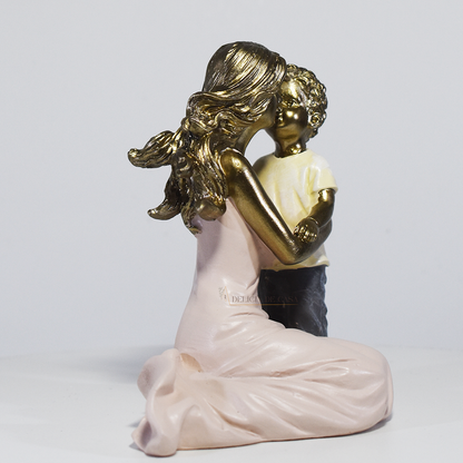 Escultura decorativa de mãe abraçando seu filho, confeccionada em resina com acabamento dourado, branco e cinza, medindo 11,5 x 11,5 x 8 cm.