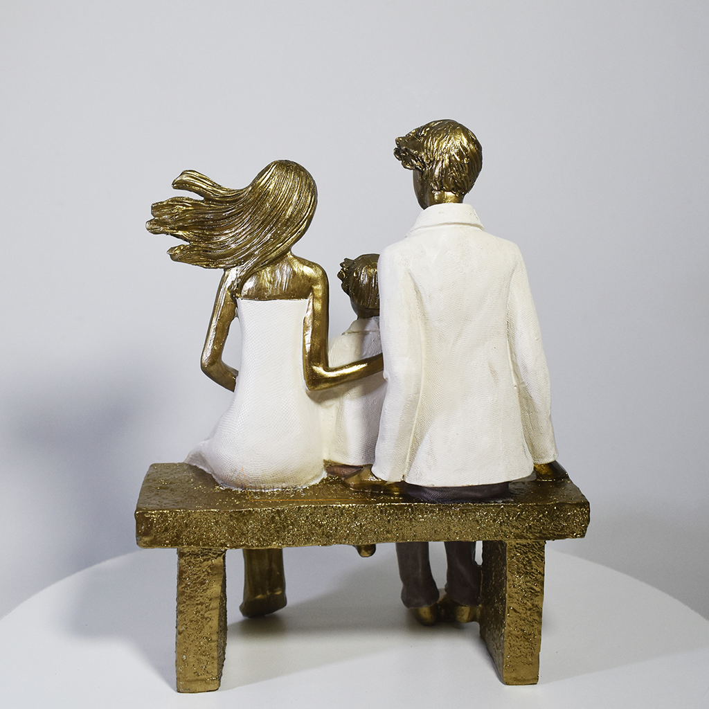 Escultura decorativa em resina representando pai, mãe e filho sentados em um banco lendo um livro, simbolizando união familiar e momentos de aprendizado.