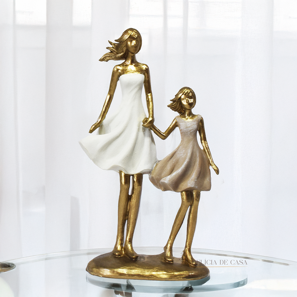 Estatueta decorativa em resina representando mãe e filha de mãos dadas, com acabamento dourado e vestidos em tons suaves. Peça elegante para simbolizar amor e conexão familiar na decoração.