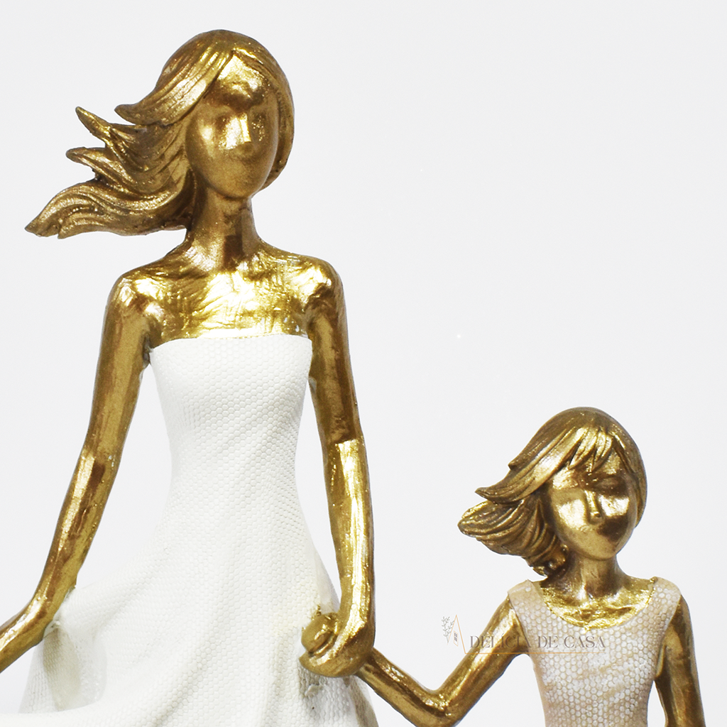 Estatueta decorativa em resina representando mãe e filha de mãos dadas, com acabamento dourado e vestidos em tons suaves. Peça elegante para simbolizar amor e conexão familiar na decoração.