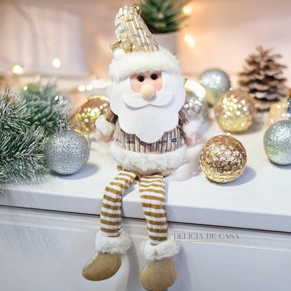 Boneco decorativo de Papai Noel sentado com pernas longas, roupas douradas e barba branca, ideal para decoração natalina em mesas e prateleiras.