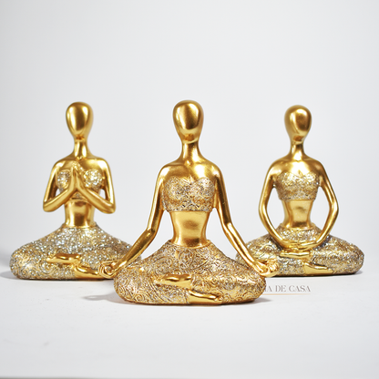 Trio de estátuas douradas com glitter representando posturas de ioga, ideal para decoração zen e ambientes de meditação.