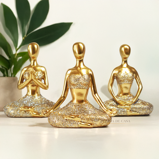 Trio de estátuas douradas com glitter representando posturas de ioga, ideal para decoração zen e ambientes de meditação.